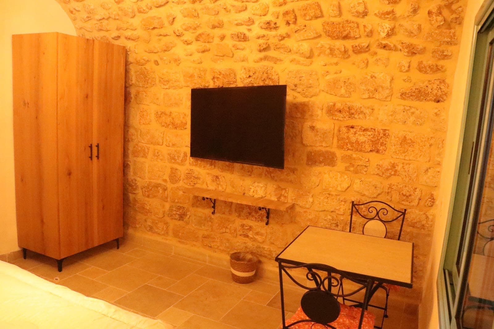 קיר אבן בחדר האירוח עם טלוויזיה תלויה, ארון עץ ושולחן קטן